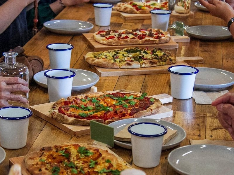 Wood-fired pizzas and enamel cups along a long lunch table